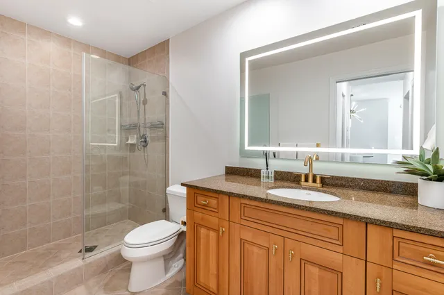 a bathroom with a granite countertop sink a toilet a mirror and shower