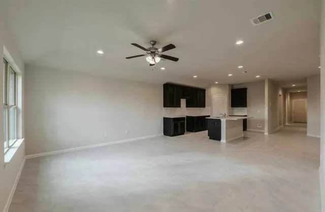 an empty room with kitchen and a ceiling fan