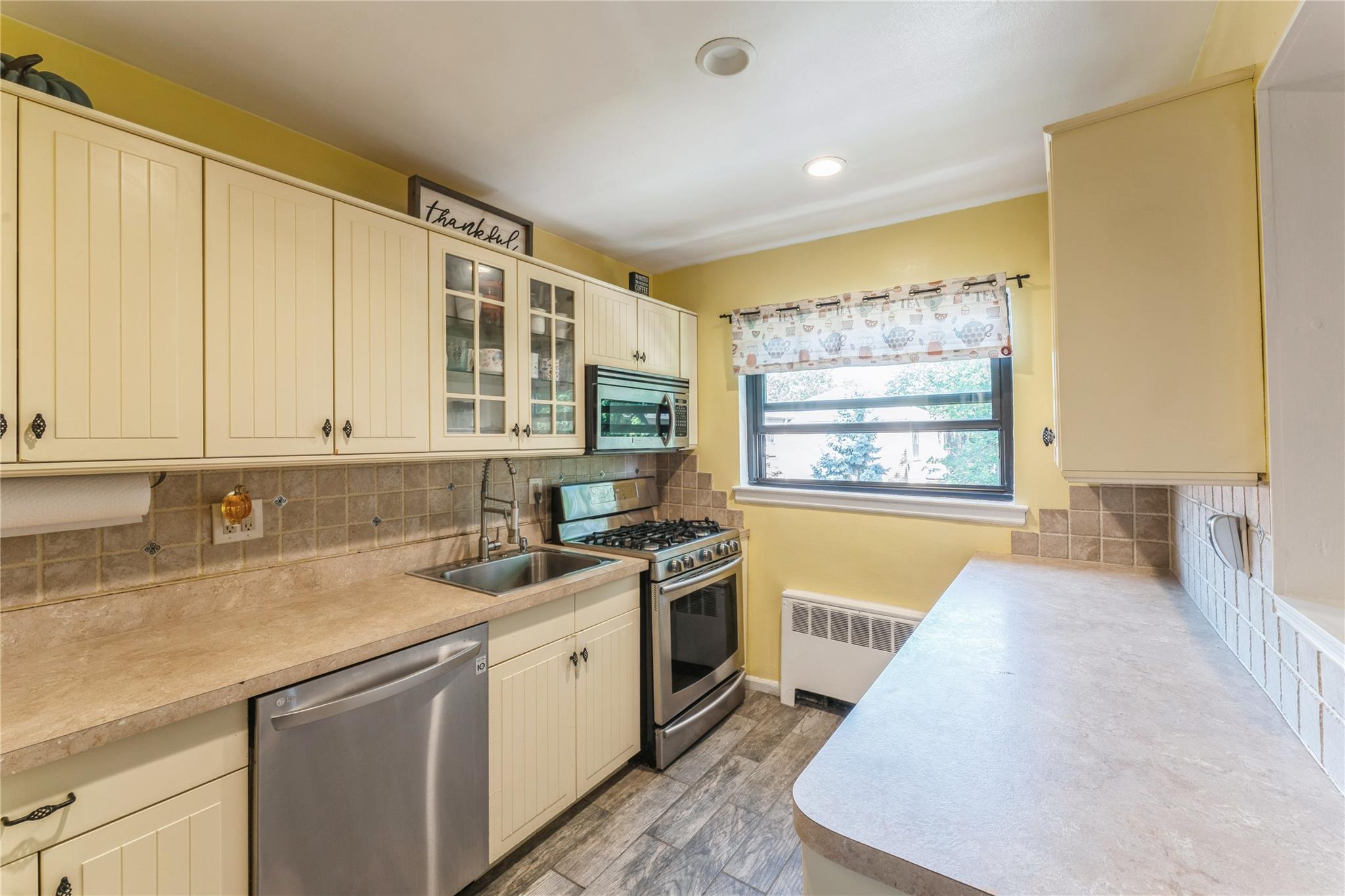 Kitchen featuring stainless steel appliances, radiator, light countertops, cream cabinets, and backsplash