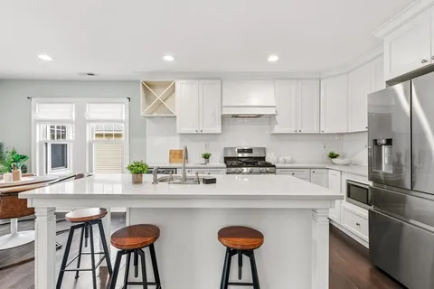 a kitchen with stainless steel appliances granite countertop a sink a stove a refrigerator and white cabinets with wooden floor