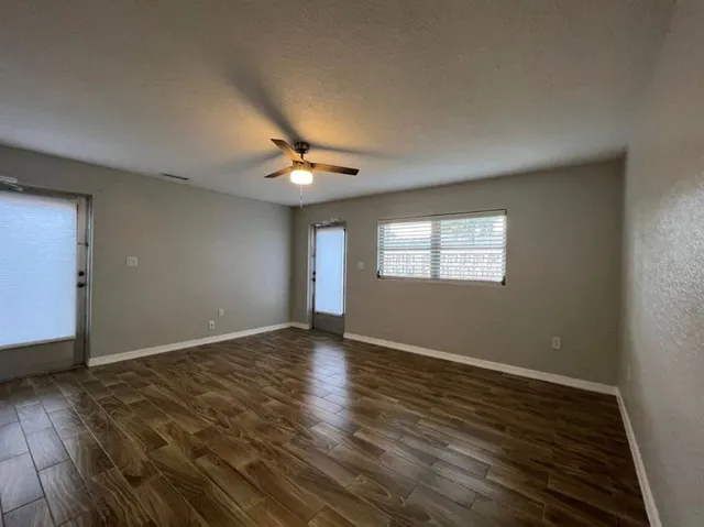 an empty room with wooden floor chandelier fan and windows