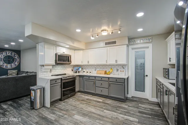 a kitchen with stainless steel appliances granite countertop a stove top oven a sink dishwasher a refrigerator and a dining table with wooden floor