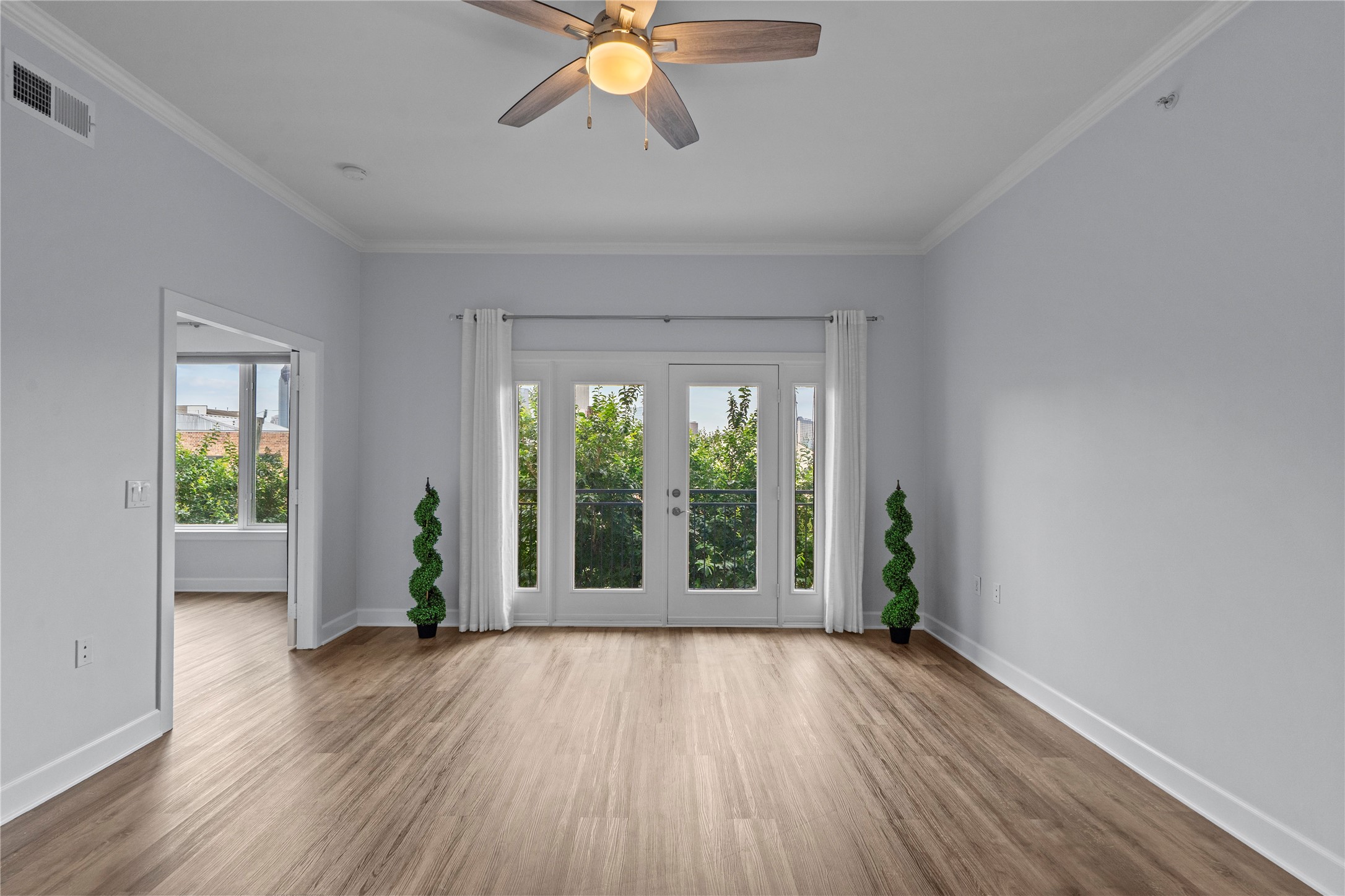 1900 Genesee Street, Unit 203 Houston, TX 77006 - Photo 2 of 30 Bright, open room with wood flooring and a ceiling fan. French doors lead to a scenic view, complemented by greenery accents. Ideal for a cozy, airy living space.