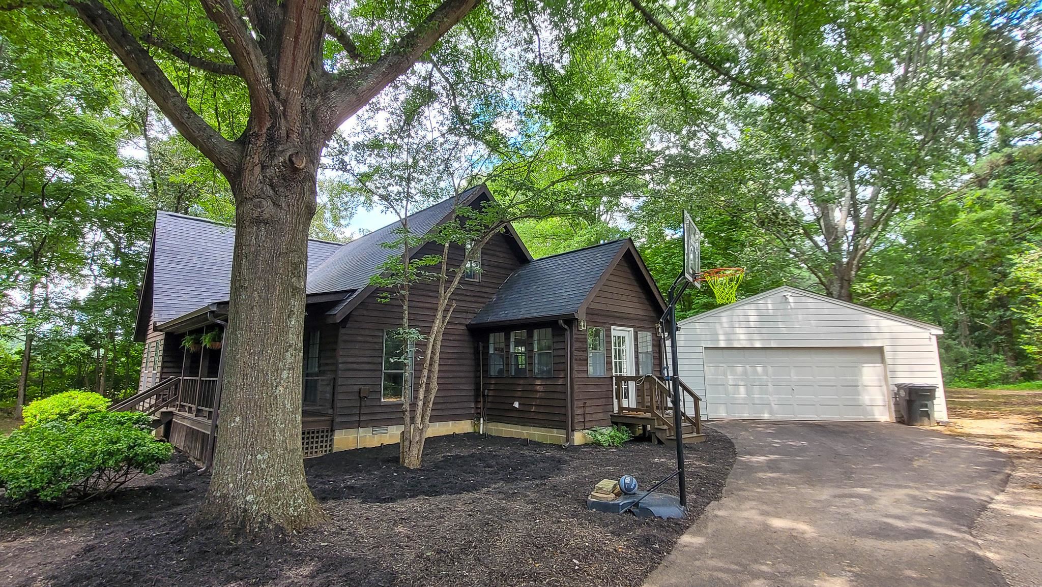 470 Rich Road Somerville, TN 38068 - Photo 10 of 40 Wood-sided residence featuring a covered porch, detached two-car garage with white overhead door, and mature trees on the property