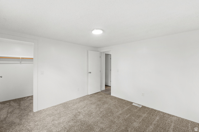 2875 North 400 West, Unit 7 Layton, UT 84041 - Photo 19 of 29 Neutral wall paint, ceiling texture, flush mount light fixture, plush carpet flooring, and an open closet with a wooden hanging rod