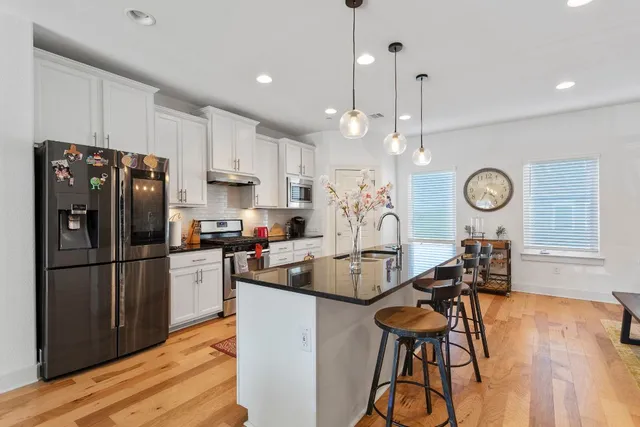 a kitchen with stainless steel appliances granite countertop a refrigerator a stove a sink a dining table and chairs with wooden floor