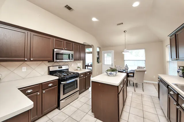 a kitchen with stainless steel appliances kitchen island granite countertop a sink a stove top oven a counter space and cabinets