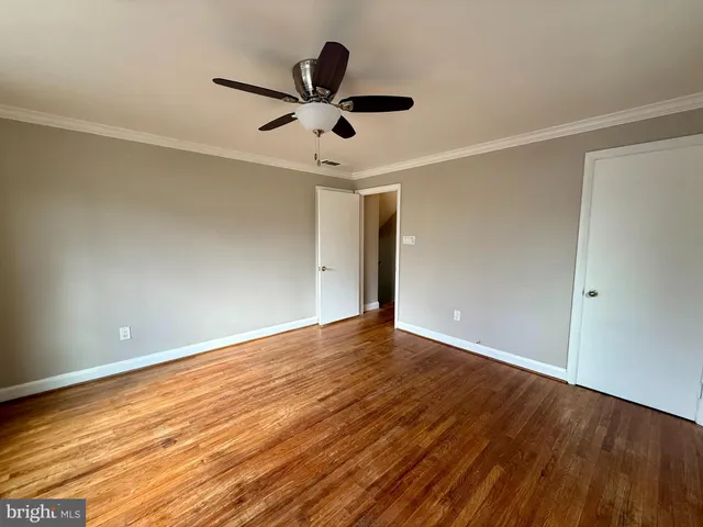 a view of an empty room with wooden floor and a ceiling fan