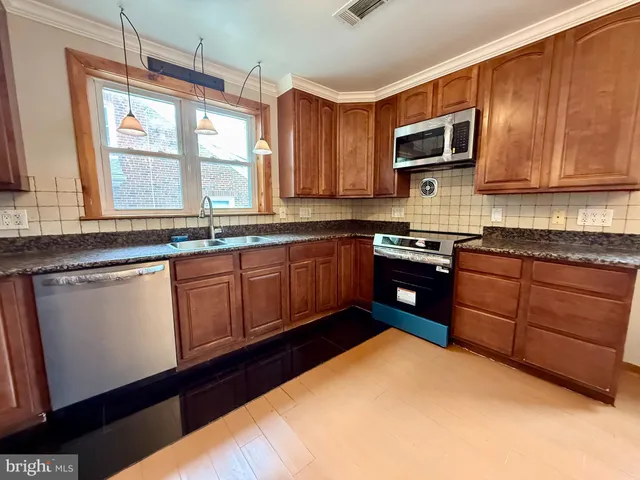 a kitchen with stainless steel appliances granite countertop wooden cabinets a sink a stove a microwave and wooden floors