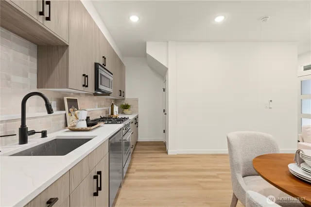 a kitchen with stainless steel appliances granite countertop a stove a sink a microwave a refrigerator white cabinets and couches with wooden floor