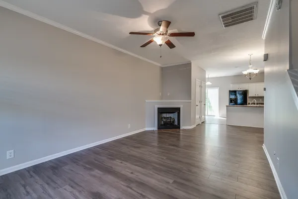 a view of an empty room with wooden floor and a kitchen