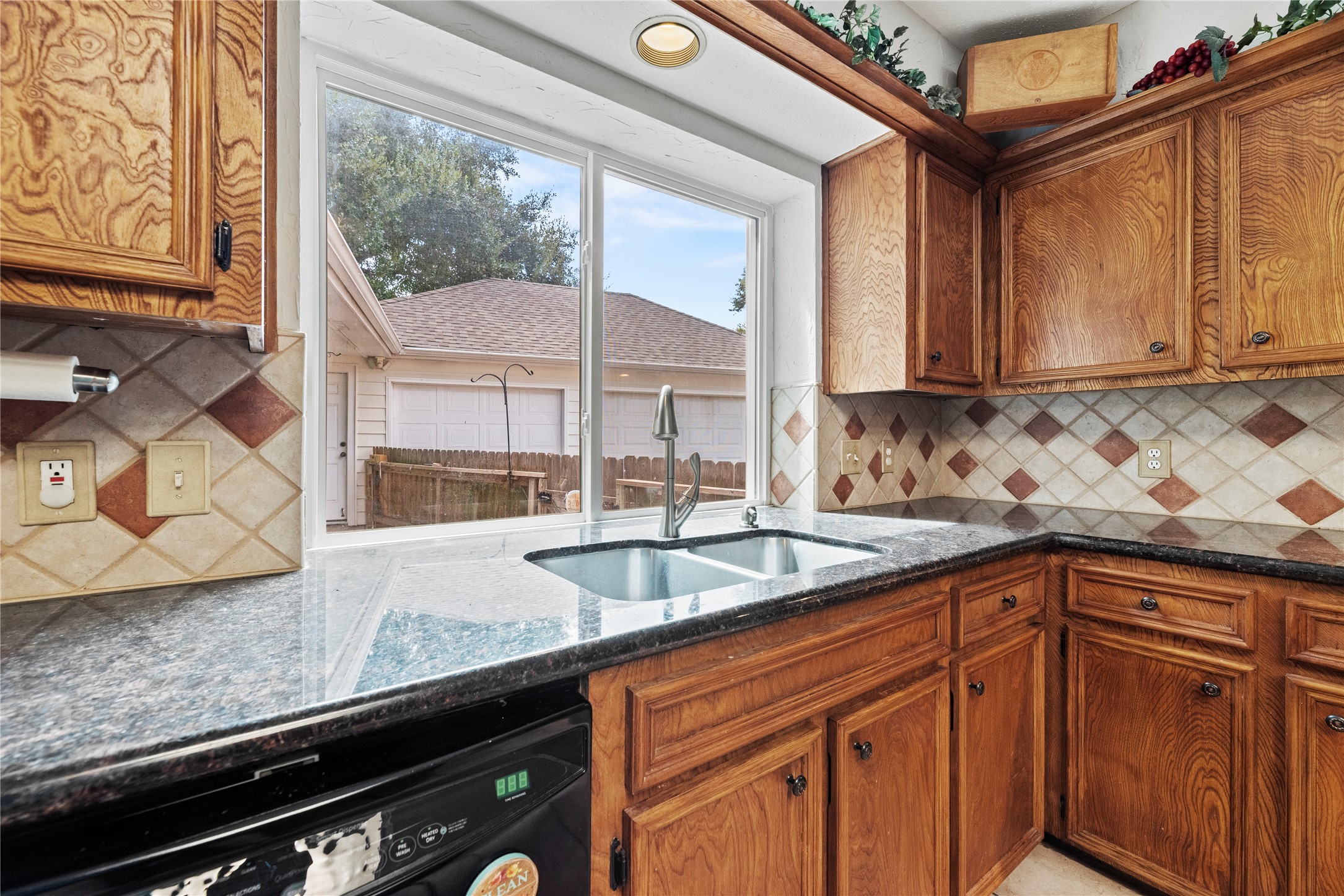 7403 Foxton Pl Court Houston, TX 77095 - Photo 14 of 41 Cleanup is easy with deep stainless steel sinks beneath a large window that looks out to the backyard, while granite countertops, rich wood cabinetry, and stylish tile backsplash bring the space together beautifully.