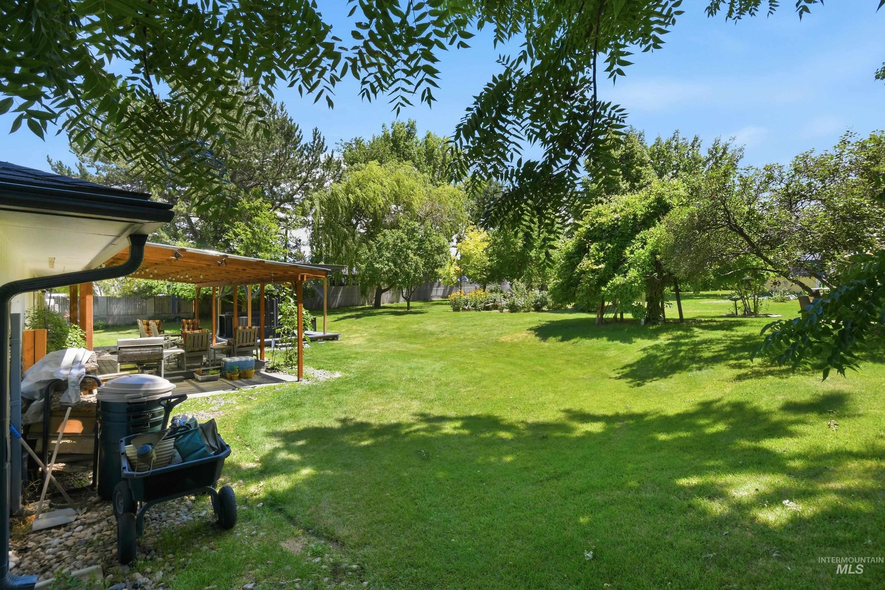15095 David Street Caldwell, ID 83607 - Photo 31 of 39 Expansive green lawn with mature trees and a dedicated patio area featuring a wooden pergola