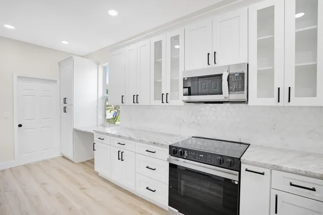 a kitchen with stainless steel appliances granite countertop white cabinets a sink a stove a microwave and wooden floors