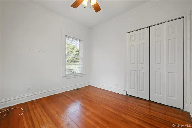 an empty room with wooden floor chandelier fan and windows