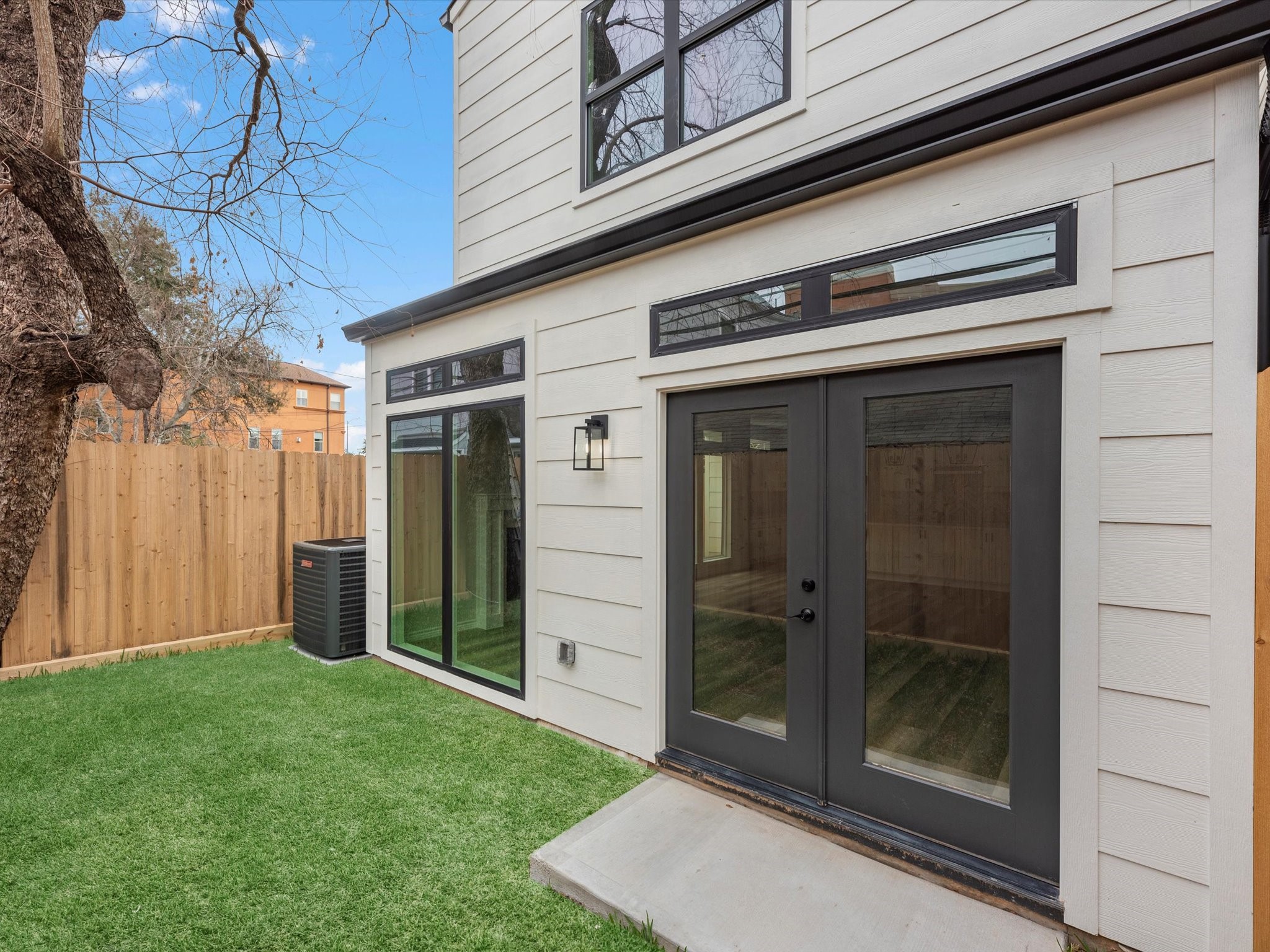 1319 West Bell Street Houston, TX 77019 - Photo 49 of 50 This photo shows a backyard with a small, private lawn. It features a wooden fence, large glass doors leading inside, and an outdoor air conditioning unit. The space is compact but well-maintained, ideal for a cozy outdoor area.