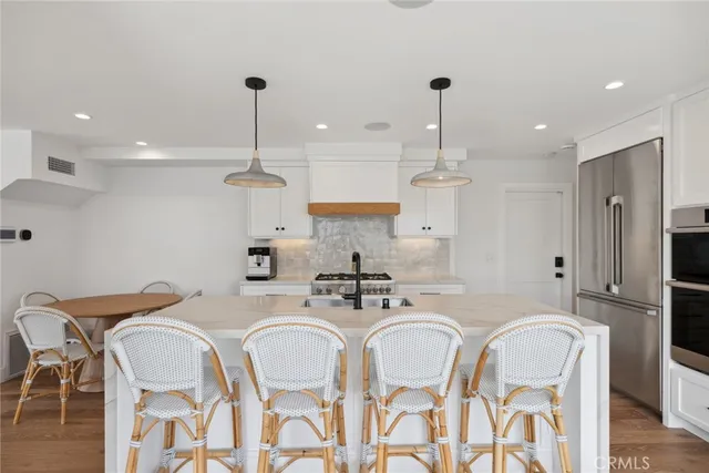 a kitchen with stainless steel appliances kitchen island granite countertop a dining table chairs and a refrigerator