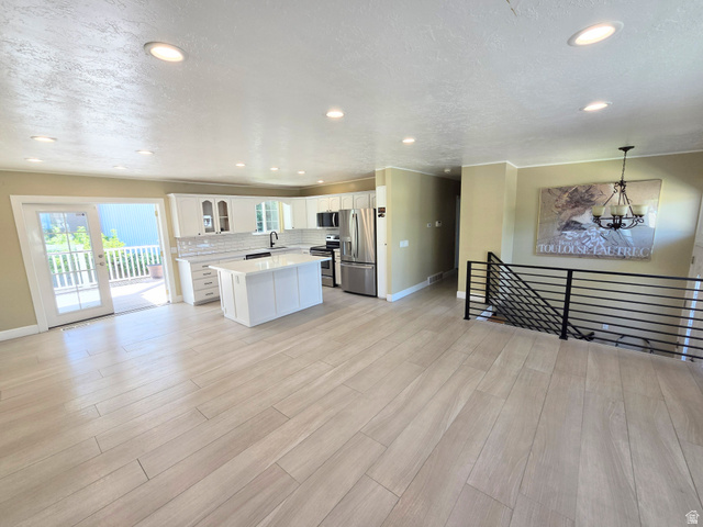6123 Rodeo Lane Murray, UT 84121 - Photo 9 of 19 Spacious open-concept living area featuring light wood-finish flooring, a contemporary kitchen with white cabinetry, a central island, and stainless steel appliances