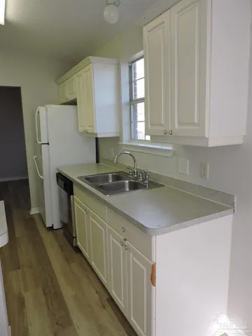 a kitchen with stainless steel appliances granite countertop a sink dishwasher a refrigerator and white cabinets with wooden floor