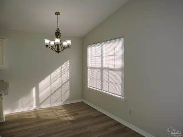 a view of an empty room with wooden floor chandeliers and a window