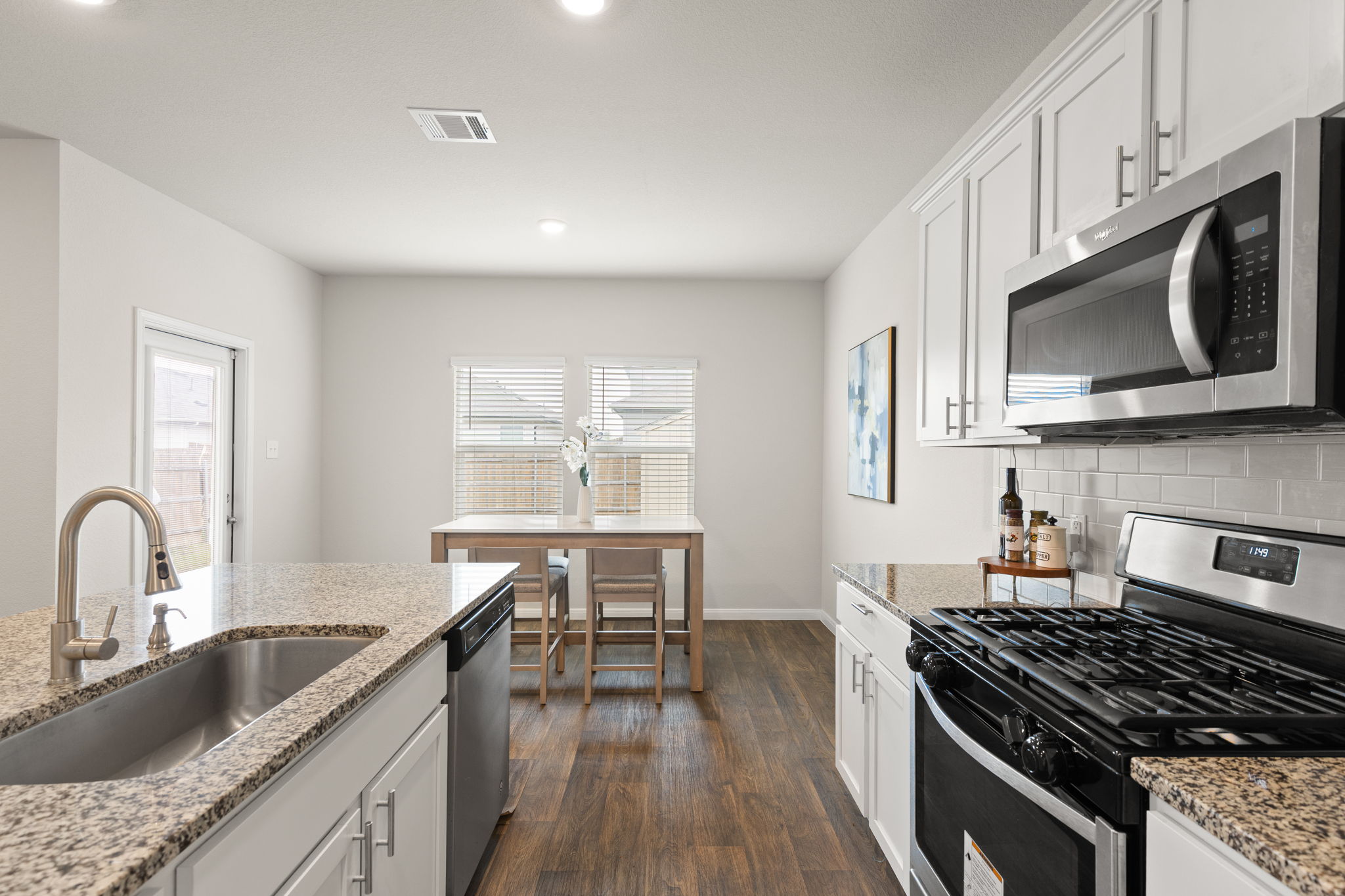 281 Jayden Drive Kyle, TX 78640 - Photo 13 of 36 Kitchen featuring granite countertops, wood-finish flooring, white cabinetry with contemporary hardware, a stainless steel sink, and a stainless steel appliance suite including a microwave and gas range