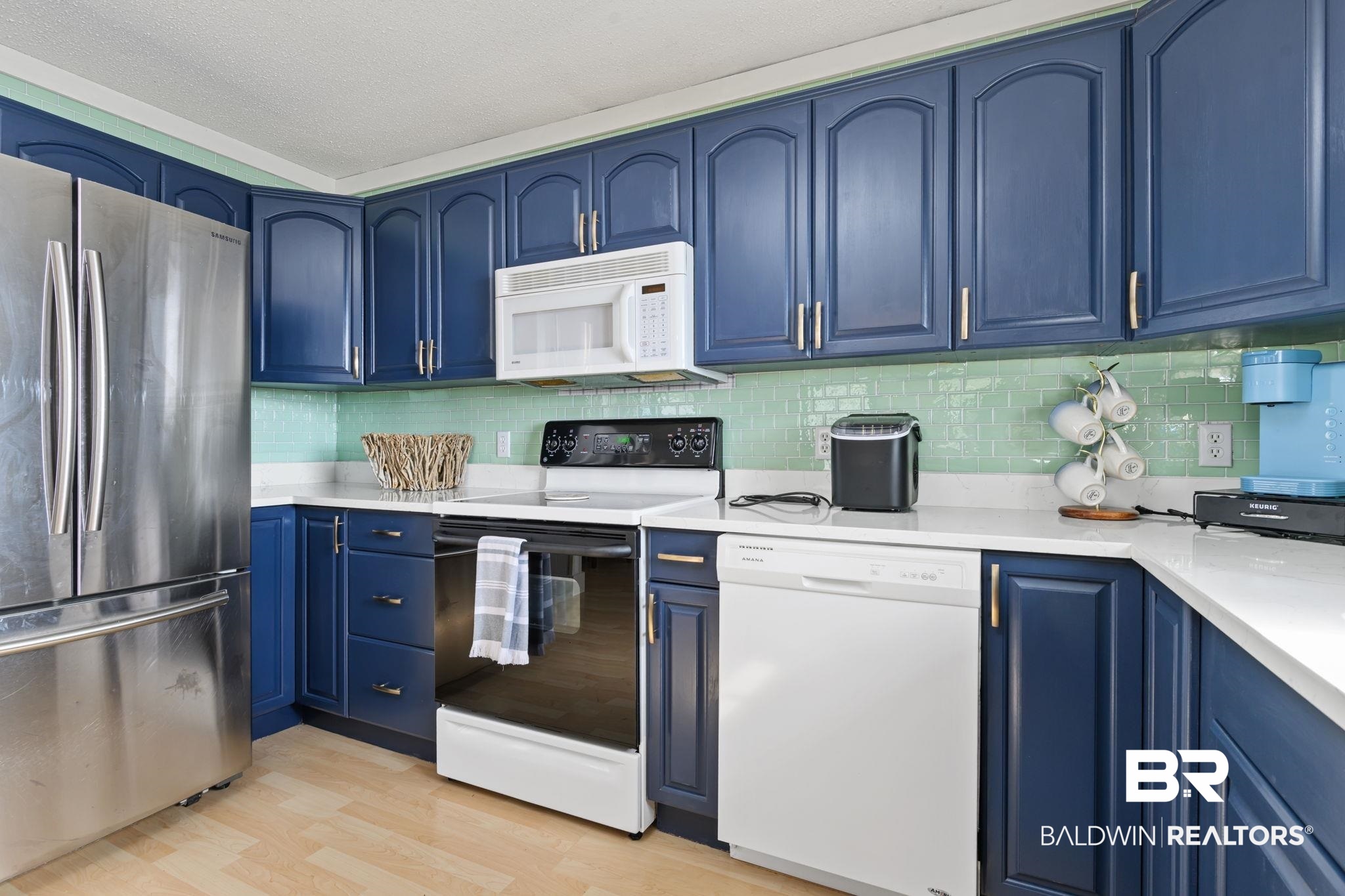 7947 Bayshore Drive Elberta, AL 36530 - Photo 16 of 26 Kitchen with blue cabinetry, white appliances, tasteful backsplash, light wood-style flooring, and light stone counters