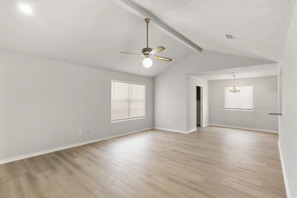 an empty room with wooden floor ceiling fan and windows