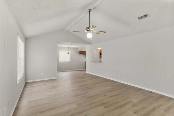 an empty room with wooden floor ceiling fan and windows