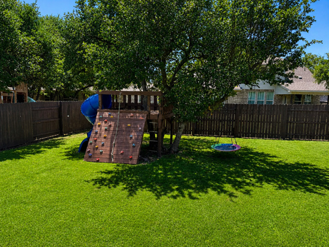 1928 Lakeside Ranch Road Georgetown, TX 78633 - Photo 35 of 37 A fenced backyard offers a playset with a climbing wall and slide, perfect for outdoor activities.