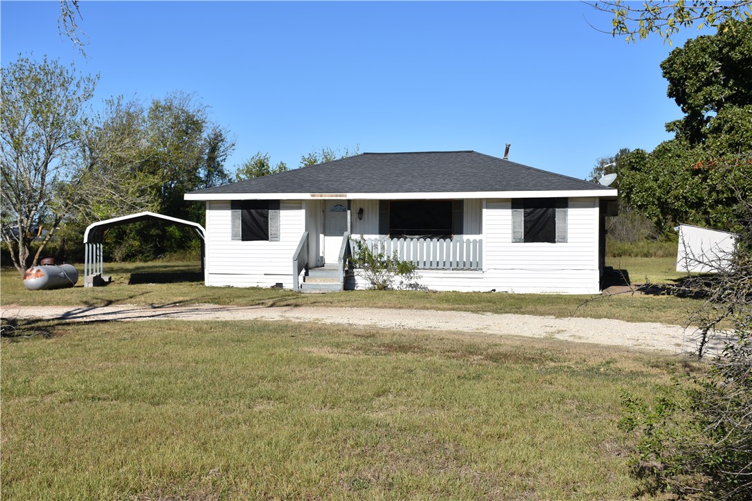 Bungalow-style house with a porch, roof with shingles, a detached carport, and a front lawn