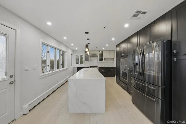 a large white kitchen with a large kitchen island stainless steel appliances wooden floor and cabinets