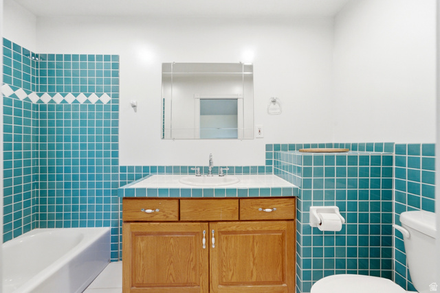 3535 Homestead Road Park City, UT 84098 - Photo 70 of 81 Bathroom featuring teal square wall tiling with a decorative white accent band, a white bathtub, a wood-finish vanity with a built-in sink, and a framed mirror