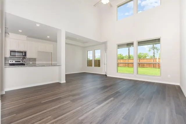 a view of an empty room with wooden floor and a kitchen
