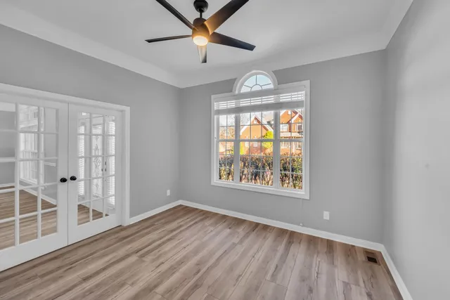 an empty room with wooden floor chandelier fan and windows