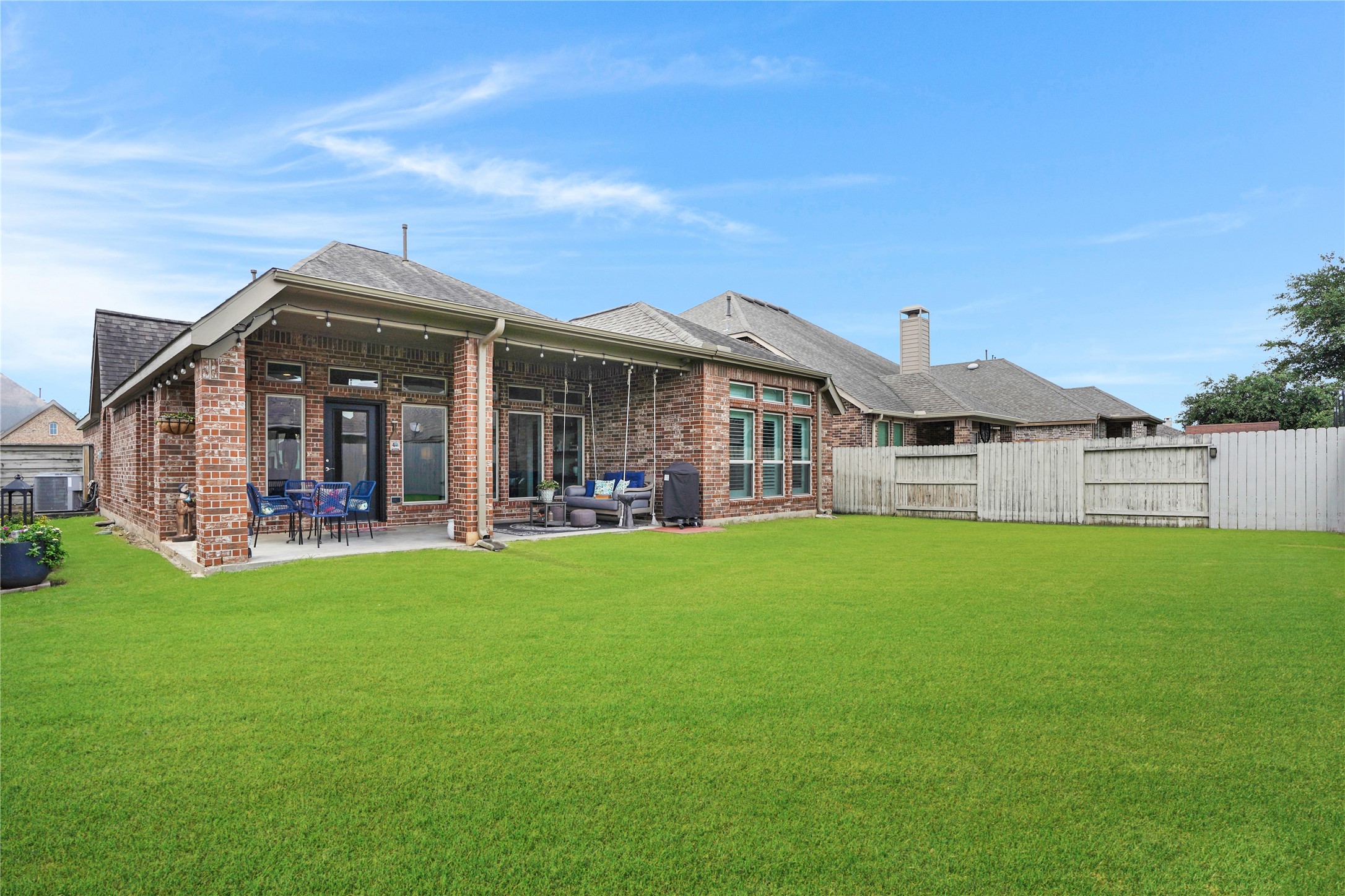 2345 Redwood Ridge Trail Manvel, TX 77578 - Photo 37 of 39 This photo showcases a spacious backyard featuring a well-maintained lawn, a covered patio with outdoor seating, and a brick exterior. Ideal for outdoor entertaining and relaxing.
