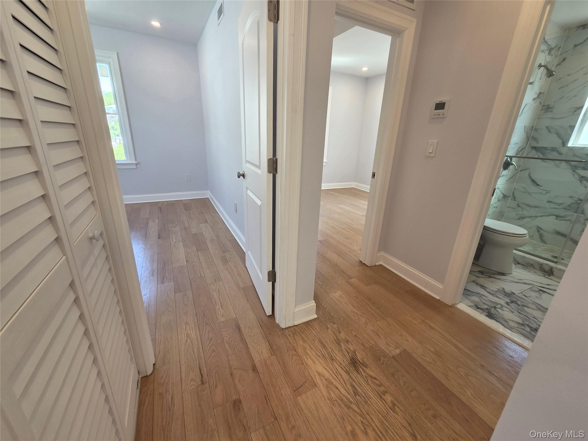 965 Main Street, Unit 2 New Rochelle, NY 10801 - Photo 12 of 12 Hardwood flooring throughout a hallway providing access to a room with a window and a bathroom with a glass-enclosed shower featuring marble-finish tile