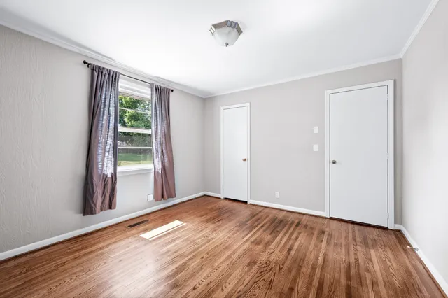 a view of an empty room with wooden floor and a window