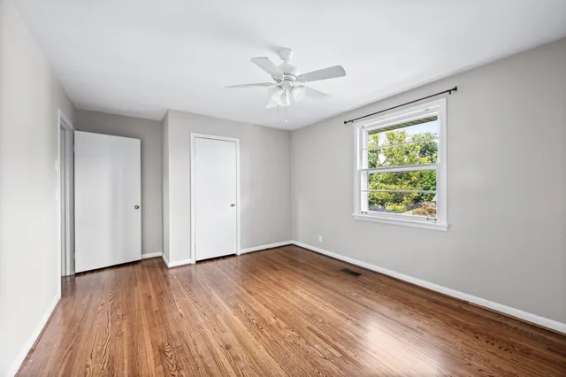 an empty room with wooden floor chandelier fan and windows