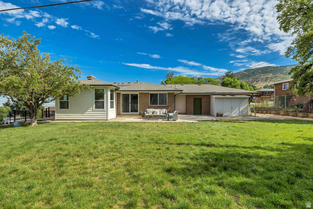1168 East Center Street Bountiful, UT 84010 - Photo 38 of 38 Expansive grassy backyard featuring a large patio area, rear brick and siding exterior, and an attached two-car garage