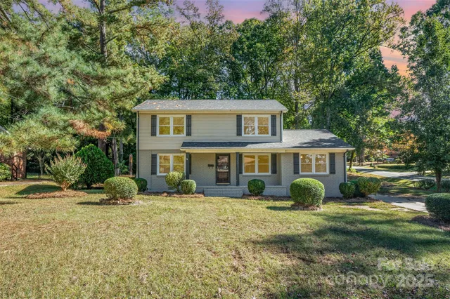 a view of a yard in front of a house with plants and large trees