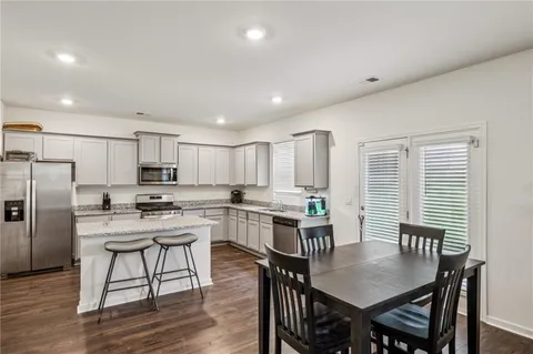 a kitchen with stainless steel appliances granite countertop a dining table chairs stove refrigerator and cabinets