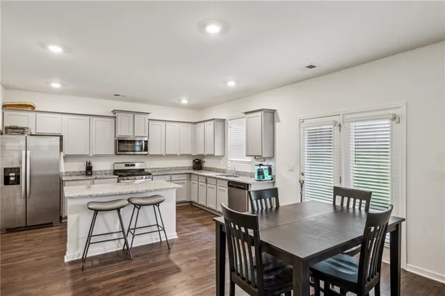 a kitchen with stainless steel appliances granite countertop a dining table chairs stove refrigerator and cabinets