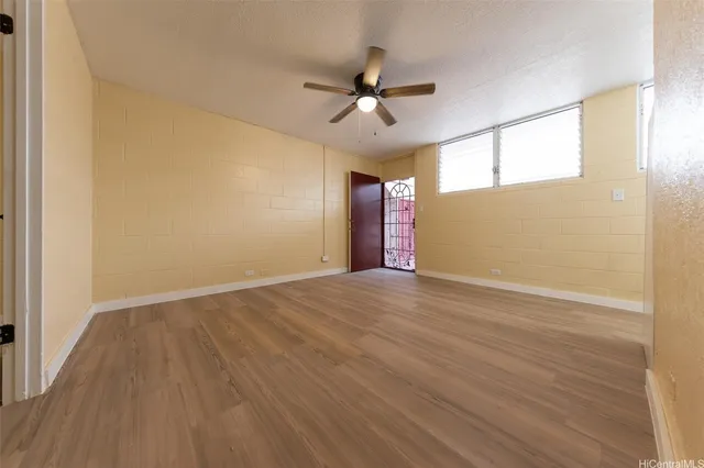 a view of an empty room with wooden floor and a ceiling fan