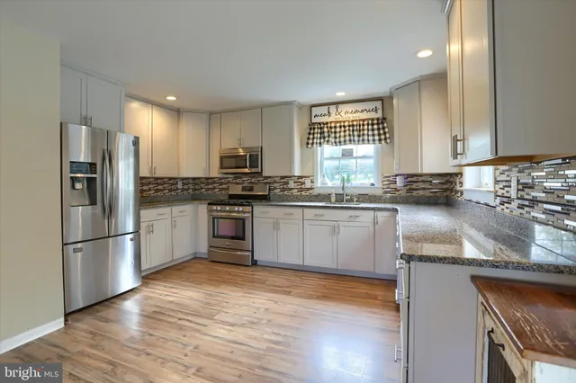 a kitchen with stainless steel appliances granite countertop a refrigerator a sink dishwasher a stove top oven a refrigerator with white cabinets and wooden floor