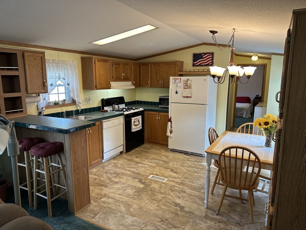 72 Quaboag Valley, Unit 70 Palmer, MA 01069 - Photo 7 of 21 a kitchen with stainless steel appliances granite countertop a stove top oven a sink a dining table and chairs with wooden floor