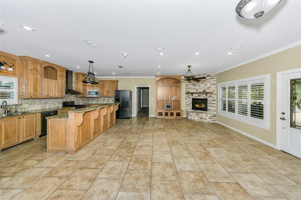566 Selma Park Road Bowie, TX 76230 - Photo 7 of 40 Expansive open-concept room featuring a kitchen with wood cabinetry and an island with bar seating, a stone-clad fireplace, and tile flooring