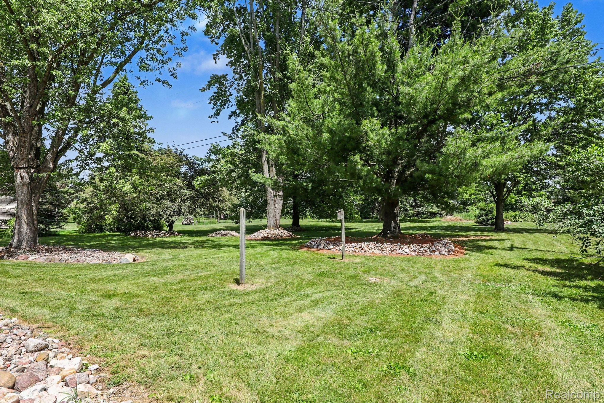 74600 Nordman Court Romeo, MI 48065 - Photo 30 of 32 Expansive lawn area featuring mature trees, mulched tree rings, and natural rock landscaping