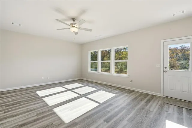 an empty room with wooden floor chandelier fan and windows