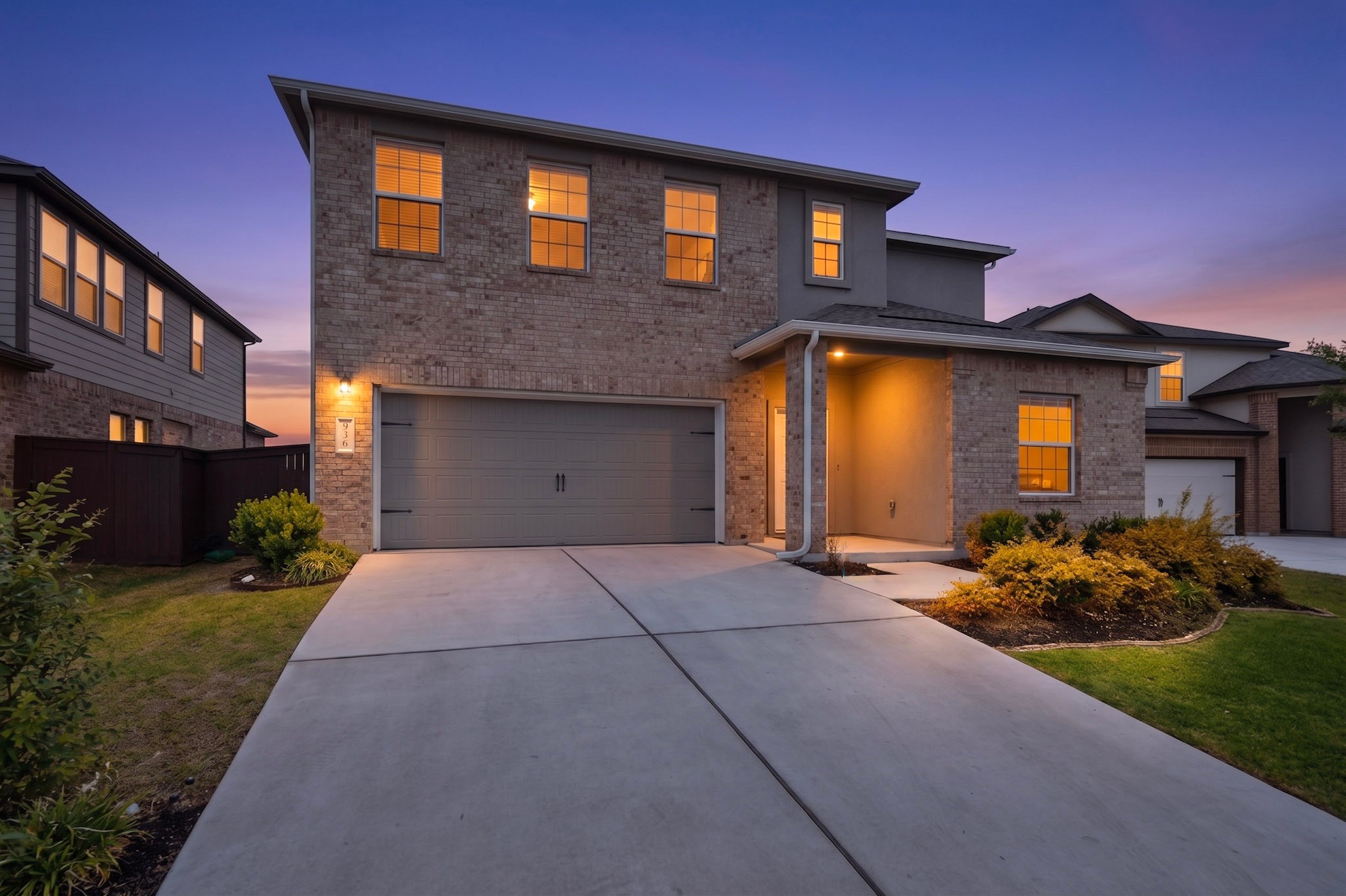 Two-story brick facade residence featuring a covered entry porch, concrete driveway, and attached two-car garage