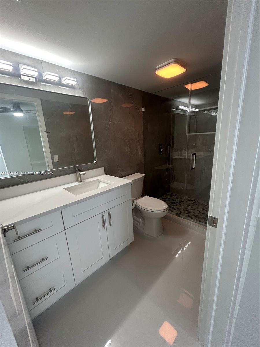 6935 Huntington Lane, Unit 107 Delray Beach, FL 33446 - Photo 13 of 23 a bathroom with a double vanity sink a toilet and a mirror